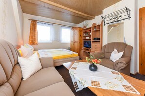 Une pièce confortable avec un canapé, un lit, une table en bois ornée d’un vase et un téléviseur posé sur une commode en bois.
