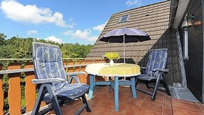A terrace with two chairs and a table, a small umbrella, and a tiled floor.
