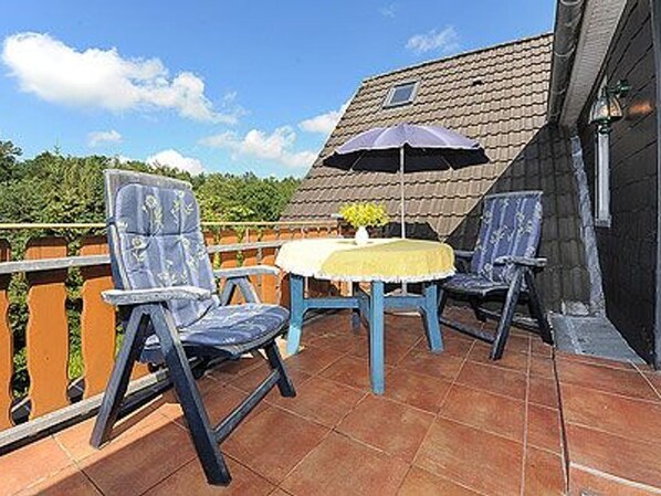A terrace with two chairs and a table, a small umbrella, and a tiled floor.
