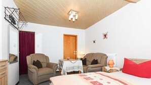 A hotel room with a bed, two chairs, a table, a wardrobe, and a door.