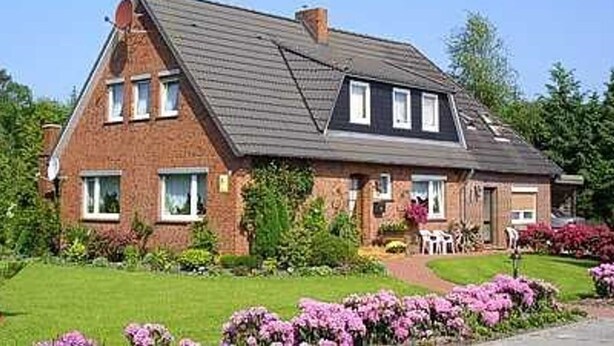A two-story house with a sloped roof, a chimney, and a front garden with flowers.