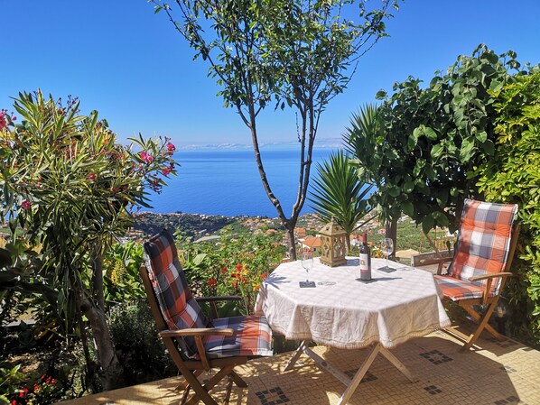 A patio with a round table and two chairs, overlooking a scenic coastal view.