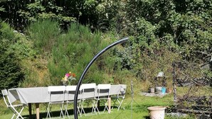 Ein runder Grill für den Außenbereich mit Metallrahmen, auf einem Kiesgrund platziert, umgeben von Grünpflanzen und einem Tisch mit Stühlen.