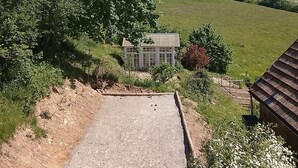 Ländliche Landschaft mit Kiesfläche, einem kleinen Gebäude und einem Haus im Hintergrund.