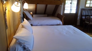 Ein Zimmer mit zwei Betten, Holzbalken, einem Fenster und einem Schreibtisch mit Stuhl.