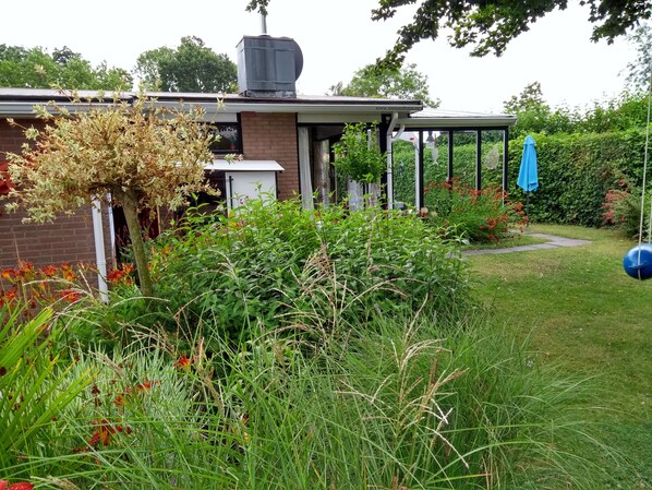 A garden with a variety of plants and flowers, a brick wall, and a covered outdoor area with a blue umbrella. - Zeelandhaus, THE house for two - sea and more (Kamperland)
