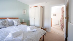 Quarto com cama, guarda-roupa, mesa de cabeceira e banheiro visível por uma porta aberta.