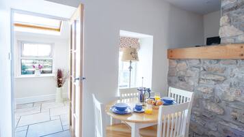 A dining area with a stone wall, a wooden table, white chairs, and a window with a view.