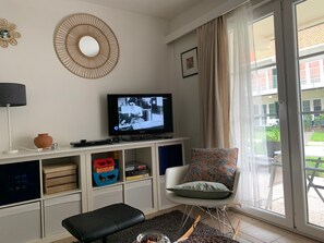 Ein Wohnzimmer mit Fernseher, einem Sessel, einer Bank und einem großen Fenster.