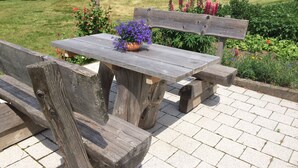 A rustic wooden bench and table set in a garden with a view of a field and distant trees. - Vacation on a farm - discover and experience nature (Baden-Württemberg)