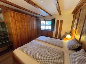 A room with two beds, wooden walls, a window with curtains, and a lamp on a bedside table. - Free: phone into german telephone network and internet-surfing with notebook (Grainau)