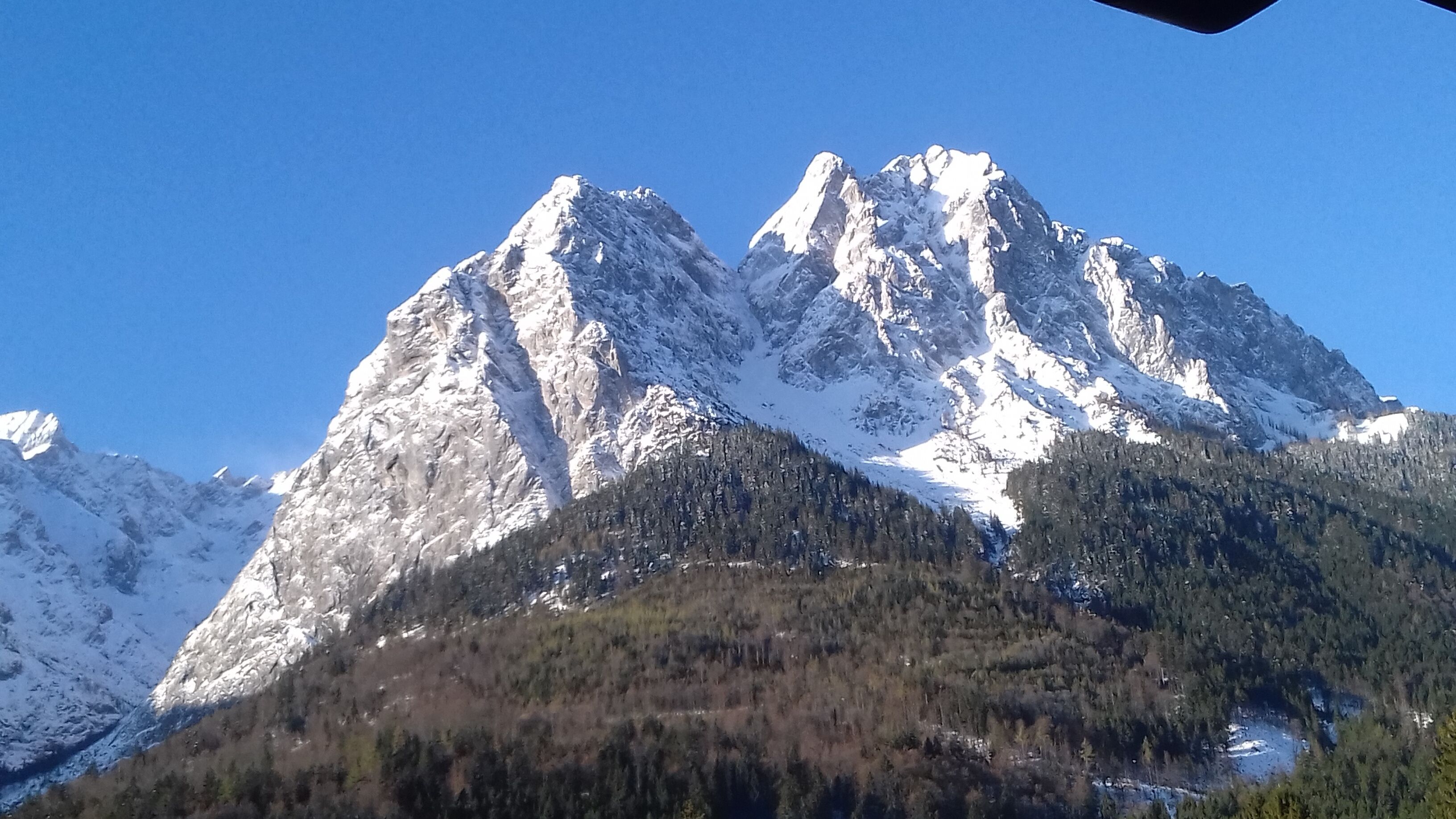 A mountain with snow-covered peaks and a forested valley.
