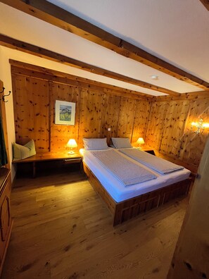 A wooden-paneled room with a bed, two bedside lamps, a bench, and a framed picture on the wall.