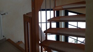 Uma escadaria espiral de madeira com corrimãos de metal, que leva a um patamar com janela com vista para um jardim.