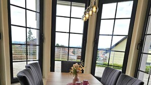 Uma sala de jantar com uma mesa de madeira comprida, cadeiras estofadas pretas, um vaso com flores e um lustre.