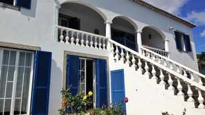 Un bâtiment aux murs blancs, aux volets bleus et à l’escalier blanc orné de balustrades.