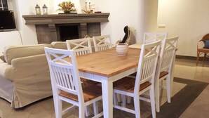 Un coin repas avec une table en bois et des chaises blanches, un canapé beige et une cheminée agrémentée d’objets décoratifs.