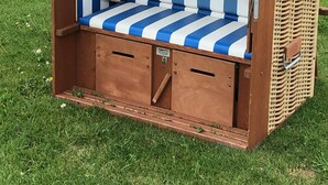 A beach chair with a striped cushion and a logo, placed on grass near a body of water. - Renner Vacation Home Behind the Dike in Spieka-Neufeld, Including a Beach Chair (Wurster Nordseeküste)