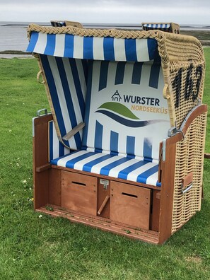 A beach chair with a striped cushion and a logo, placed on grass near a body of water.