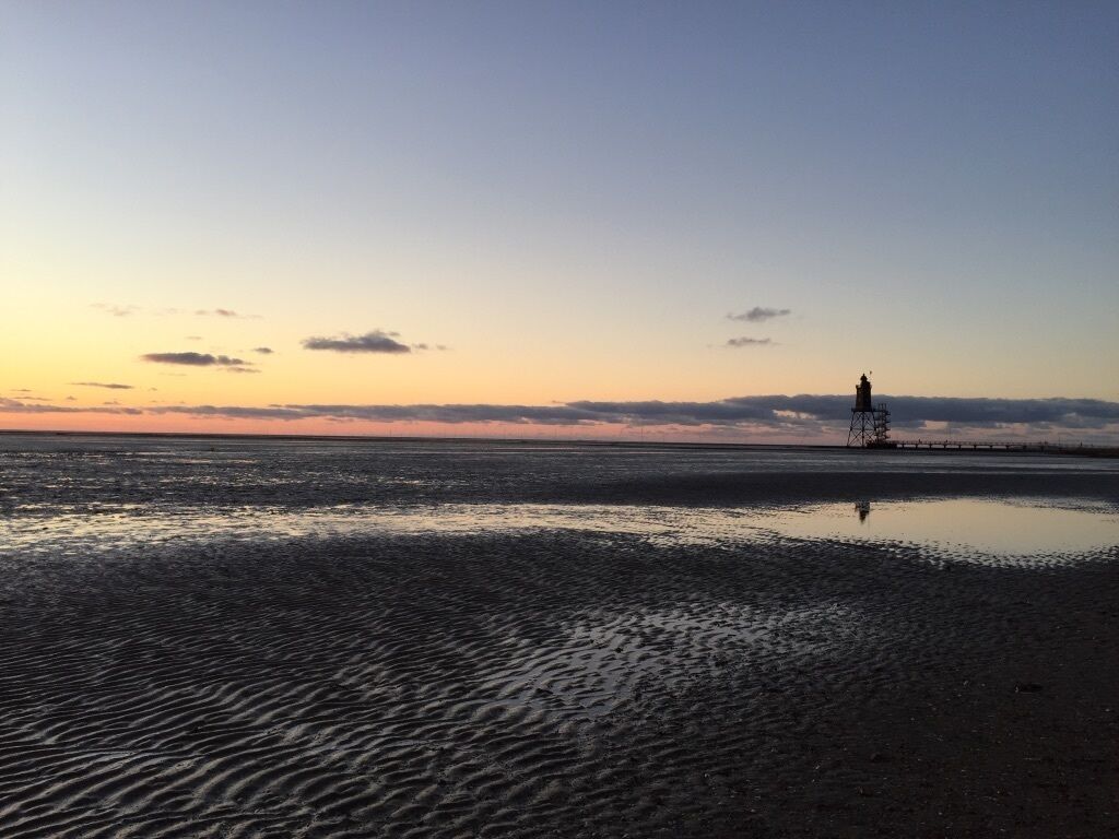 A beach with a lighthouse in the distance, calm water, and a clear sky.