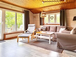 A cozy living room with a wooden ceiling, a sofa set, a chair, and a coffee table.