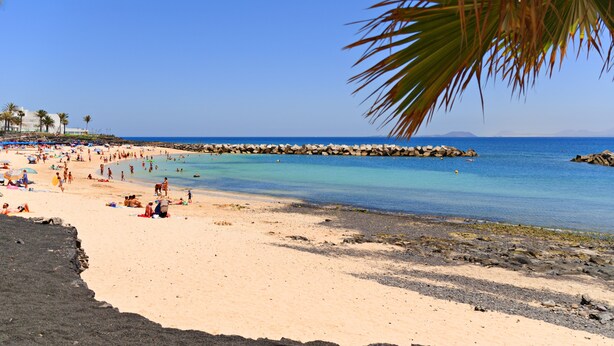 Une plage animée, avec de l’eau d’un bleu limpide et une digue rocheuse.