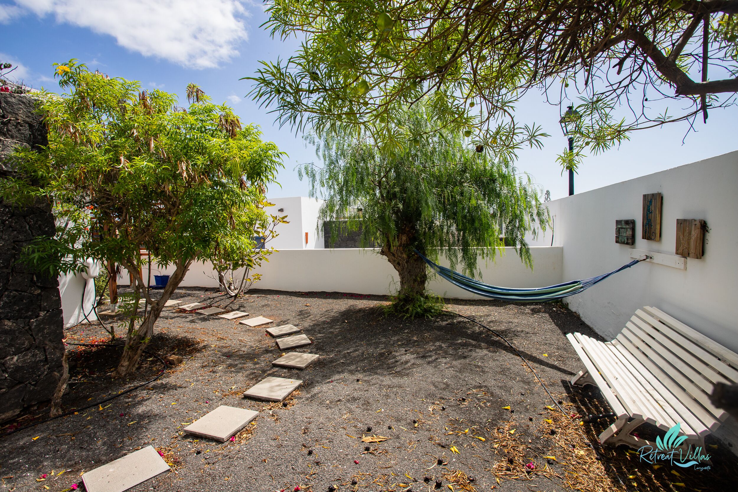 A garden area with a hammock, a white bench, and a tree.