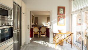 Eine moderne Küche mit Edelstahlgeräten, ein Essbereich mit Tisch und Stühlen sowie ein Ausblick durch ein großes Fenster.