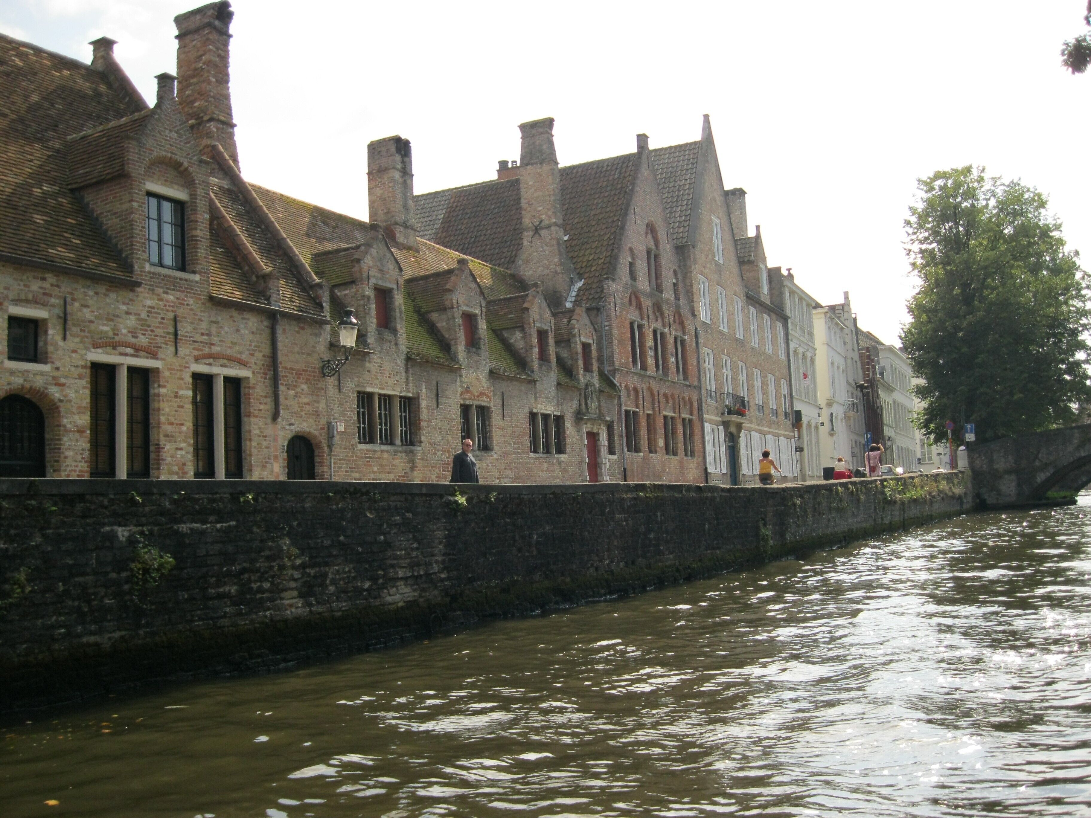 A historic building with a stone facade, multiple chimneys, and a waterway adjacent to it.