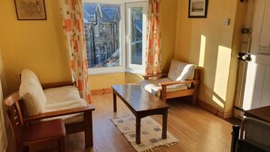 A cozy room with a wooden floor, a sofa, a chair, a small table, and a window with curtains.