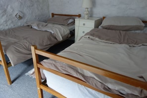 A room with two wooden beds, a white nightstand with a lamp, and a white wall with peeling paint.
