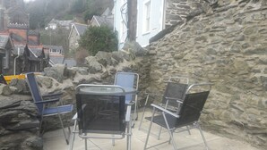 A stone wall with metal chairs and a table, a blue building, and a church in the background.