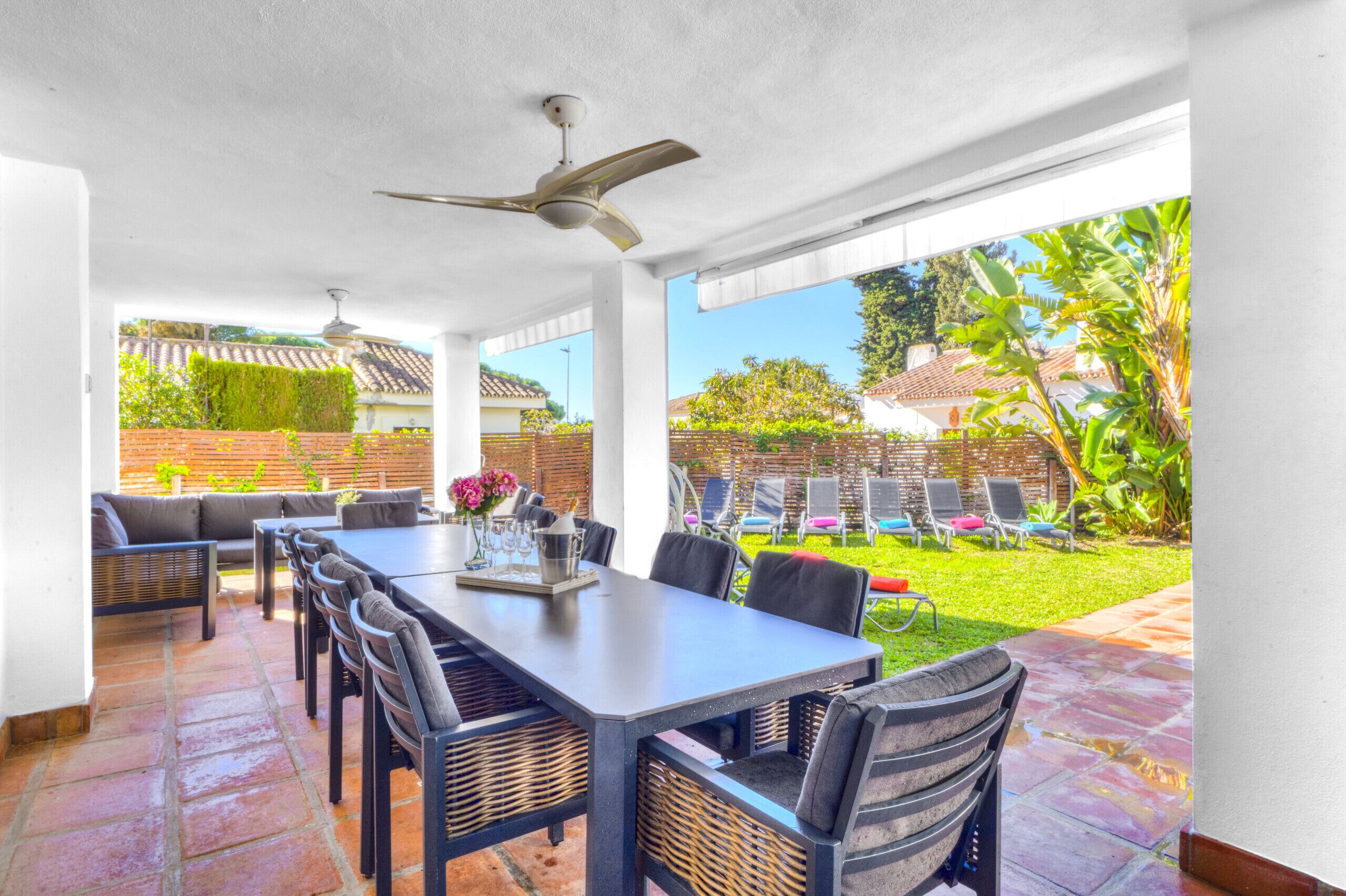 An outdoor patio with a dining table and chairs, a ceiling fan, and a view of a backyard with a pool and lounge chairs.