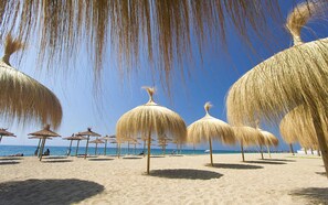 Een strand met rieten parasols en een helderblauwe lucht.