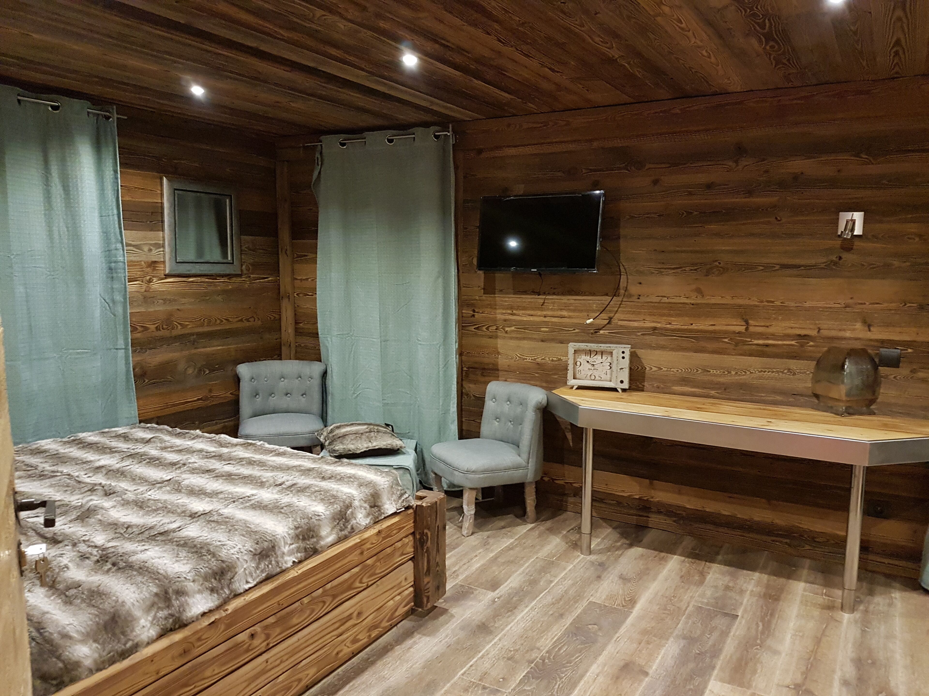 Una habitación acogedora con una cama, dos sillones, un escritorio y un televisor instalado en la pared.