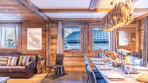 A rustic wooden interior with a long dining table set for a meal, a leather sofa, and a wooden chair.
