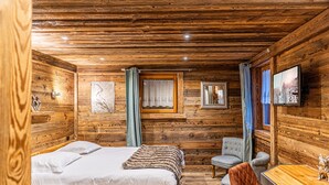 A wooden cabin room with a bed, two chairs, a table, and a window with curtains.