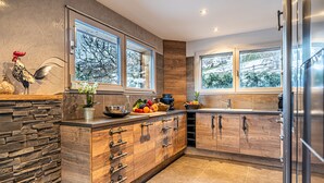 A modern kitchen with wooden cabinets, a stone accent wall, and large windows offering a view of trees.