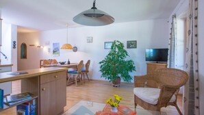 Una sala de estar moderna con comedor, una planta grande en maceta, un televisor y una silla de mimbre.