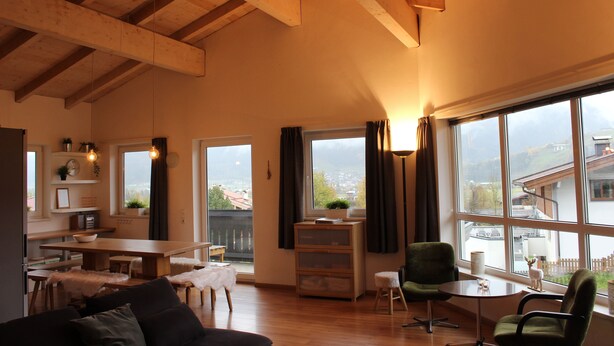 Amplia sala de estar con techo de madera, una mesa de comedor, un sofá y vistas al exterior a través de grandes ventanales.
