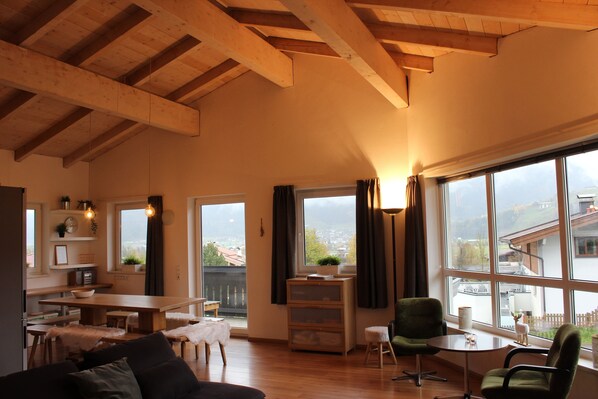 A spacious living area with a wooden ceiling, a dining table, a sofa, and a view of the outside through large windows. - Chalet Bergbach: ultimate holiday feeling in your own home! (Piesendorf)
