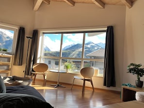 A room with a large window, wooden floor, a bed, two chairs, a small table, and a potted plant. - Chalet Bergbach: ultimate holiday feeling in your own home! (Piesendorf)