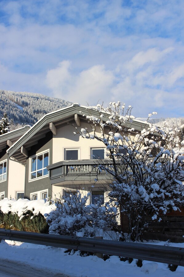 Een meerhoog gebouw met een balkon, omgeven door met sneeuw bedekte bomen en een bergachtig landschap.