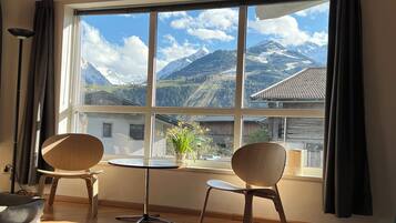 A room with a large window, two chairs, a small table, and a lamp.