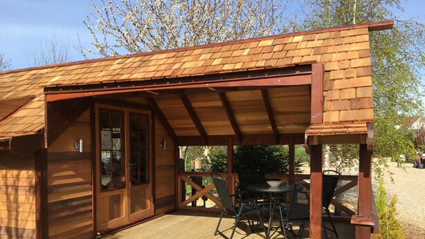 A wooden cabin with a covered patio, a sliding glass door, and a small outdoor table and chairs.