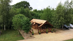 A wooden cabin with a sloped roof, surrounded by trees and a gravel driveway.