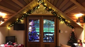 A cozy room with a wooden ceiling, a Christmas tree, and a TV on the wall.