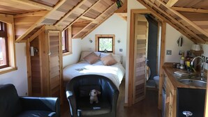 A cozy room with a bed, a black leather chair, a small table, and a kitchenette area.