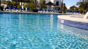 A clear pool with blue tiles, lounge chairs, and palm trees.