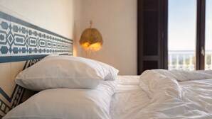 A bed with white bedding and pillows, a patterned headboard, and a hanging light fixture.